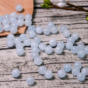 May include: A scattering of light blue round beads on a textured surface. The beads are smooth and have a slight translucence.