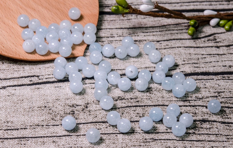 May include: A scattering of light blue round beads on a textured surface. The beads are smooth and have a slight translucence.