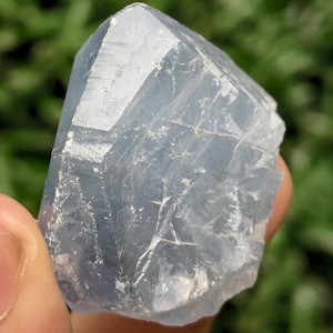 Może przedstawiać: Półprzezroczysty, jasnoniebieski okaz kryształu celestynu ze spiczastym, fasetowanym zakończeniem. Minerał charakteryzuje się naturalną, nieregularną strukturą geometryczną z widocznymi wewnętrznymi pęknięciami, ostrymi krawędziami oraz gładką, szklistą powierzchnią.