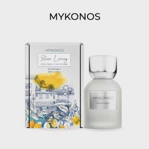Könnte beinhalten: Ein Mykonos Slow Living Eau de Parfum 50ml Flakon und die dazugehörige rechteckige Schachtel. Die Schachtel zeigt eine gelb-blaue Illustration eines Küstengebäudes mit Zitronen. Der Flakon ist opak weiß mit silbernem Verschluss und Etikett.