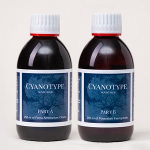 May include: Two bottles of Cyanotype sensitizer, Part A and Part B, each containing 250 ml of liquid. The bottles have white labels with blue text and a tree design. The bottles have white caps with red rings.