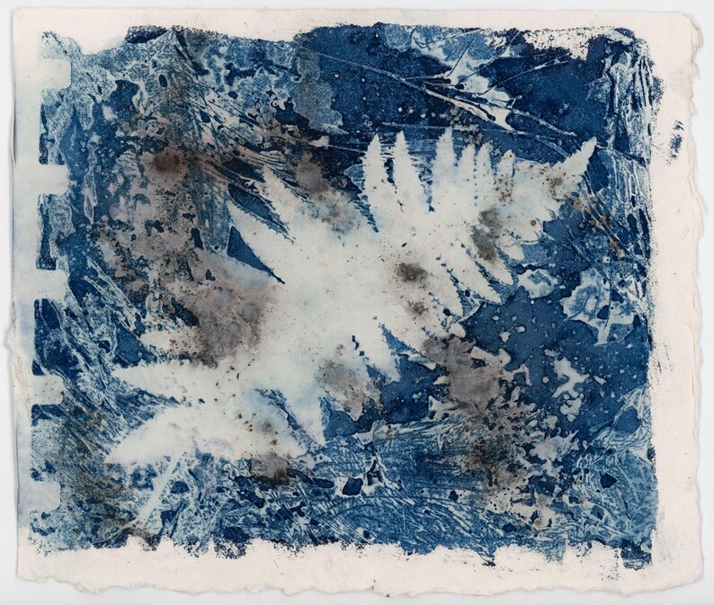 May include: Abstract cyanotype print featuring a central white fern-like shape against a textured background of deep blue and gray hues. The edges of the paper are rough and uneven, adding to the artwork's unique aesthetic. The print has a vintage, handmade feel.