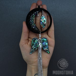 May include: A black beaded crescent moon dreamcatcher with a green abalone shell pendant and a silver angel charm with abalone wings and a chain tassel.