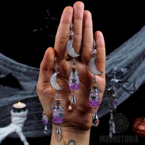 May include: Three silver crescent moon charms with dangling glass bottles filled with purple and white glitter. Each bottle has a silver star charm and a crystal teardrop charm.