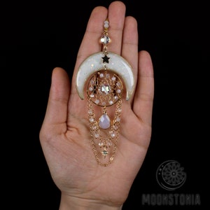 May include: A white crescent moon with a gold star and a crystal dreamcatcher pendant with a pink teardrop charm and gold chains.