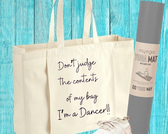 May include: A white canvas tote bag with the text "Don't judge the contents of my bag I'm a Dancer!!" printed on it. A gray yoga mat with the text "myoga YOGA MAT WITH CARRY STRAP GO YOUR WAY" is on the right side of the image. A white and gray sneaker is on the bottom right of the image.