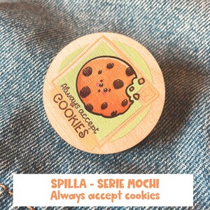 Op de afbeelding: Een ronde houten pin met een cartoon-koekje erop. Het koekje heeft chocolade chips en een hap eruit. De tekst "Always accept COOKIES" staat op de pin.
