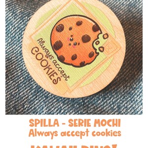 Op de afbeelding: Een ronde houten pin met een cartoon-koekontwerp. De koek heeft chocolade-chips en een groene frosting-beet. De tekst "Always accept cookies" staat rond de koek. De pin is op een blauwe denim-achtergrond.