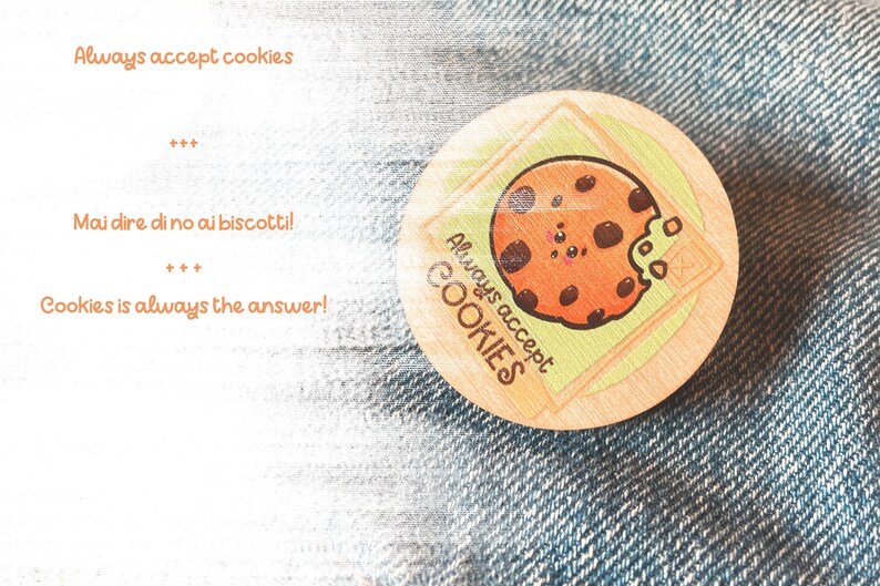 Op de afbeelding: Een ronde houten pin met een cartoon-cookie-ontwerp. De cookie heeft chocolade chips en een glimlachend gezicht. De tekst "Always accept COOKIES" staat rond de cookie. De pin is op een blauwe denim achtergrond.