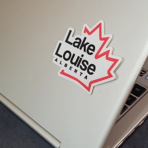 May include: A white sticker with a red maple leaf outline and the text "Lake Louise Alberta" in black lettering.