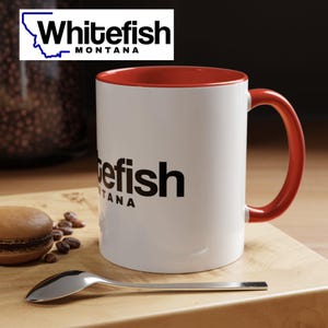 May include: White ceramic mug with a red rim and handle. The mug has a black graphic of the text "Whitefish Montana" on the front.