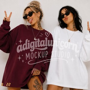 May include: Two oversized crewneck sweatshirts, one in deep burgundy and one in crisp white, featuring long sleeves and a relaxed fit. The garments are plain with no visible patterns or prints, worn with simple silver pendant necklaces.