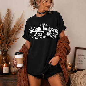 May include: A black short-sleeved t-shirt featuring white graphic text that reads adigitalunicorn MOCKUP STUDIO with a small heart and star accents. The shirt is worn with a thick, chunky, rust-colored knit cardigan and black shorts.