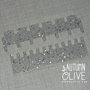 May include: Two clear acrylic strips featuring a silver glitter finish and embedded star-shaped sequins. The top strip has five wide rectangular tabs, while the bottom strip has ten narrower rectangular tabs. The text AUTUMN OLIVE is visible.