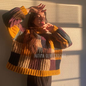 Könnte beinhalten: Ein Patchwork-Häkelpullover in Senfgelb, Lila, Marineblau und Beige. Der Pullover hat eine gerippte Textur, einen Rollkragen und lange Ärmel. Der Text "AUTUMN OLIVE CROCHET" ist sichtbar.