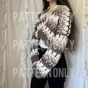 May include: A brown and white crocheted cropped cardigan with a V-neck and long sleeves. The cardigan is made with a textured stitch and has a loose fit.