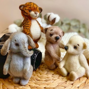 Puede incluir: Cuatro juguetes de peluche hechos a mano: un tigre, un elefante y dos osos. El tigre es naranja y negro con rayas blancas. El elefante es gris con una trompa larga. Un oso es marrón y el otro es blanco. Los juguetes están sentados en una cesta tejida.
