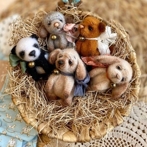 Puede incluir: Cinco pequeños animales de peluche en una cesta tejida llena de paja. Los animales incluyen un panda, un perro, un conejito, un oso y un animal gris con orejas grandes. Cada animal tiene una pequeña campana atada al cuello.