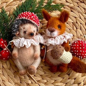 Può includere: Due giocattoli di peluche fatti a mano, un riccio con un cappello a fungo rosso e bianco e uno scoiattolo con un colletto a volant bianco, che tiene una ghianda marrone. Entrambi i giocattoli sono seduti su una superficie di vimini intrecciato.