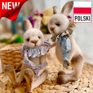 Pode incluir: Dois coelhos de pelúcia feitos à mão com pelo marrom claro, usando colares florais azuis e brancos. Os coelhos estão sentados em uma superfície de vime tecida.