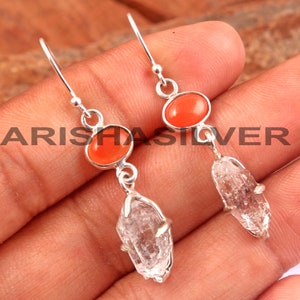 May include: Silver dangle earrings with a clear quartz crystal and an orange carnelian gemstone.