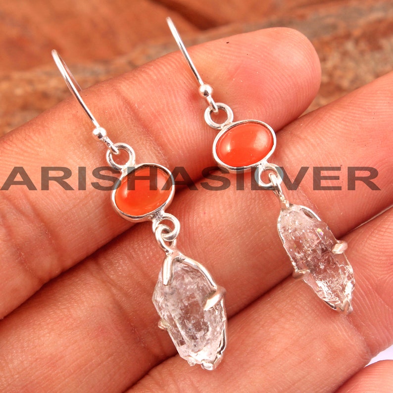 May include: Silver dangle earrings with a clear quartz crystal and an orange carnelian gemstone.