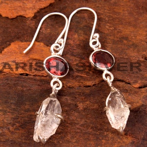 May include: A pair of silver earrings with red gemstone accents and clear crystal drops.