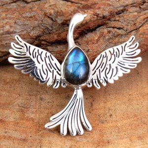 May include: Silver pendant featuring a bird with outstretched wings and a blue labradorite gemstone in the center.