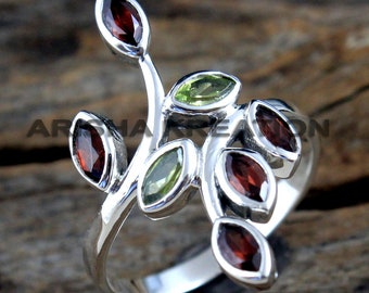 Può includere: Un anello d'argento con un design a forma di ramo con pietre preziose verdi e rosse. L'anello ha un aspetto delicato e organico.