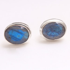 Puede incluir: Un par de pendientes de botón de plata con piedras de labradorita azul de forma ovalada.