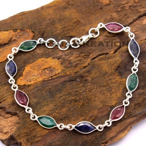 May include: A silver chain bracelet with alternating green, blue, and red gemstone accents. The gemstones are oval-shaped and have a faceted finish.