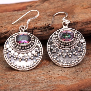 May include: Silver earrings with a round, ornate design and a rainbow-colored gemstone in the center.