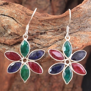 Puede incluir: Un par de pendientes de plata con diseño de flor. Los pendientes tienen seis piedras preciosas en forma de flor, con tres piedras verdes, dos rojas y una azul.