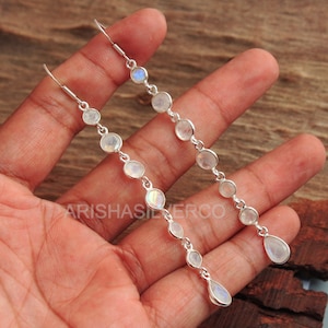 May include: A pair of long silver dangle earrings with moonstone beads. The earrings have a teardrop-shaped moonstone at the bottom.
