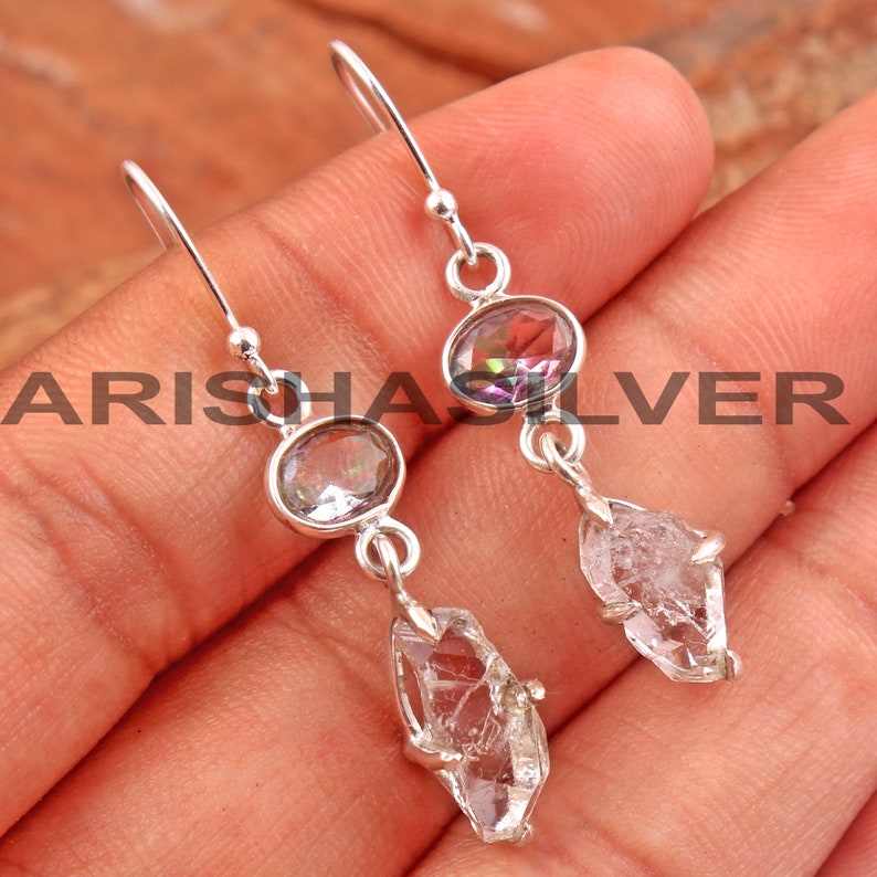 May include: Silver dangle earrings with a clear crystal and a rainbow iridescent oval gemstone.