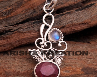 Pode incluir: Um pingente de prata com um rubi vermelho e uma pedra de lua branca. O pingente tem a forma de um desenho floral com folhas e volutas.