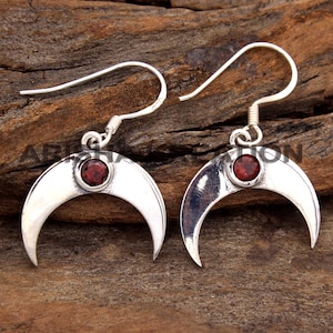 May include: A pair of silver crescent moon earrings with red gemstone accents.