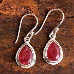 Peut inclure: Une paire de boucles d'oreilles pendantes en argent avec des pendentifs en forme de larme en pierre rouge. Les boucles d'oreilles ont un design simple avec un crochet en argent et un sertissage en forme de larme pour la pierre précieuse.