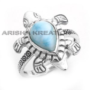 Op de afbeelding: Zilveren schildpadring met een blauwe en witte iriserende edelsteen. De ring heeft een gedetailleerd ontwerp en is een prachtig sieraad.