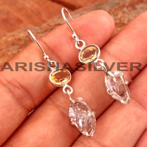 May include: Silver dangle earrings with a clear quartz crystal and a yellow oval gemstone.