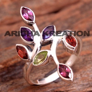 May include: Silver ring with a branch design featuring five gemstones: amethyst, peridot, and garnet. The ring has a delicate, intricate design.