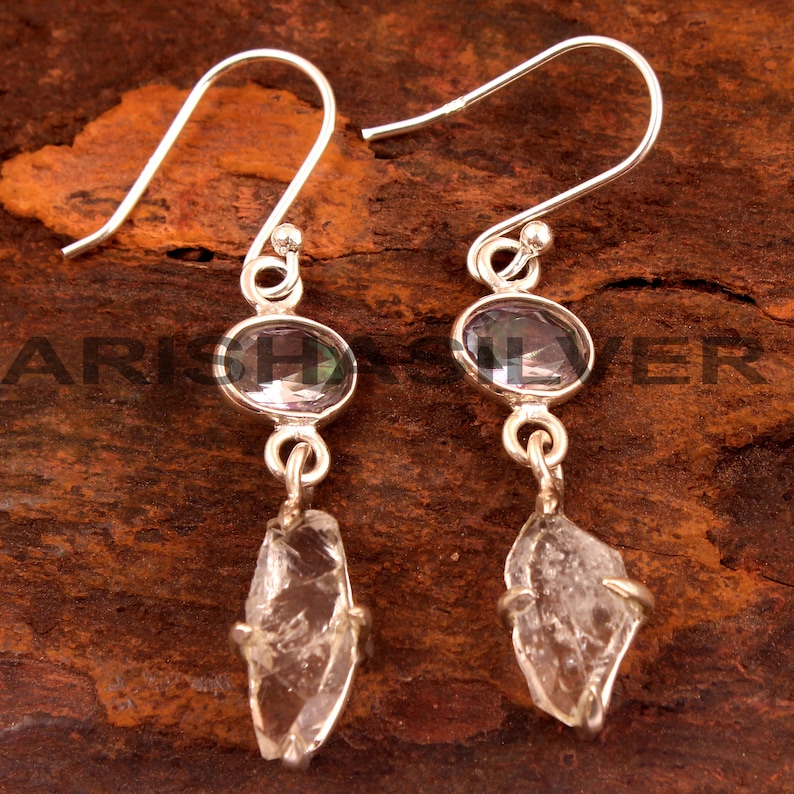 May include: Silver dangle earrings with a clear quartz crystal and a purple oval gemstone.