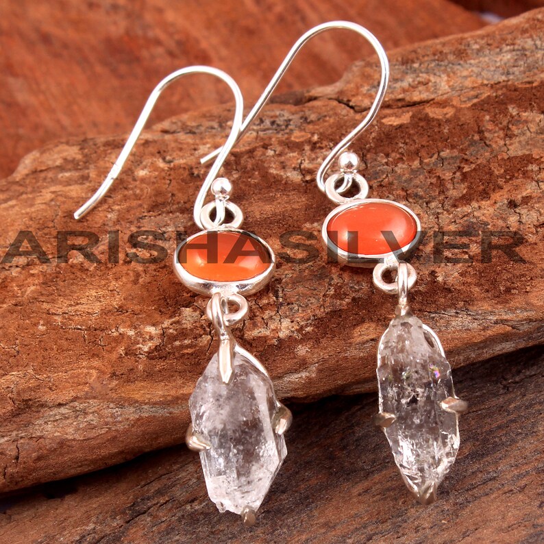 May include: Silver earrings with a teardrop-shaped clear crystal and a round orange gemstone.