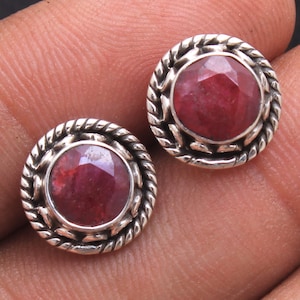 以下が含まれることがあります： 赤い宝石がそれぞれにセットされた、銀製のイヤリングのペア。イヤリングは、セッティングの縁にロープのようなデザインが施されています。