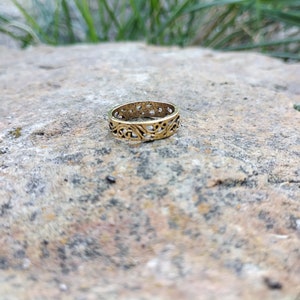 Puede incluir: Un anillo de color dorado con un diseño delicado e intrincado. El anillo está hecho de metal y tiene una forma circular.