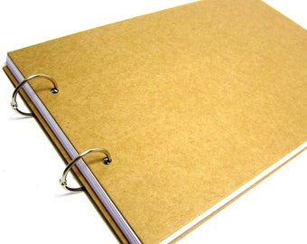 May include: A brown cardboard scrapbook with three silver rings for holding pages. The scrapbook is closed and lying on a white surface.