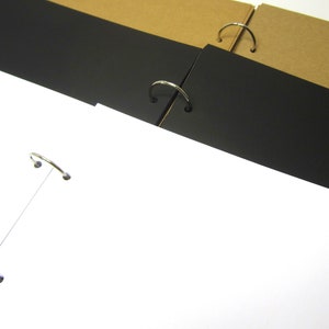 May include: A white, blank page with three black pages bound together with silver rings. The pages are stacked on top of each other.
