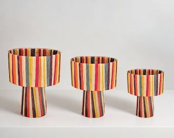 May include: Three colorful striped woven baskets with a pedestal base. The baskets are different sizes and are made of natural materials.