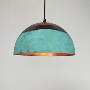 Op de afbeelding: Een hanglamp met een koperkleurig interieur en een turquoise buitenkant. Het bovenste gedeelte is donkerbruin van kleur. Het licht hangt aan een zwart snoer en is aan het plafond bevestigd.
