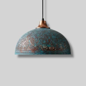 Puede incluir: Lámpara colgante de color turquesa con parte superior de cobre y patrones calados detallados. La lámpara cuelga de un cable negro, ofreciendo una solución de iluminación decorativa y funcional. La pantalla en forma de cúpula tiene un acabado envejecido.
